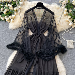 Black lace lingerie set with feathered sleeves on a hanger, surrounded by decorative flowers and fur.