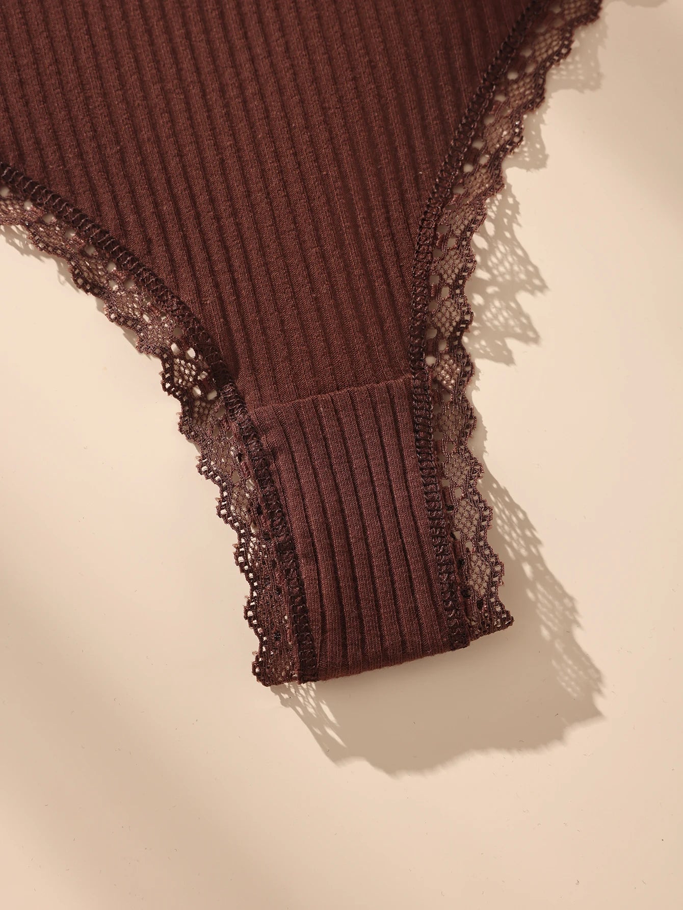 Brown ribbed garment with lace trim on a beige background