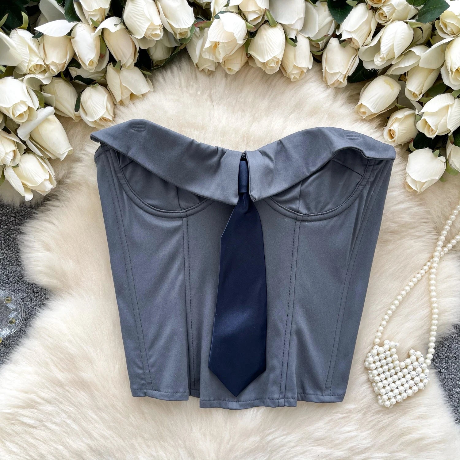 Gray top with a blue tie on a white fur surface with white flowers in the background