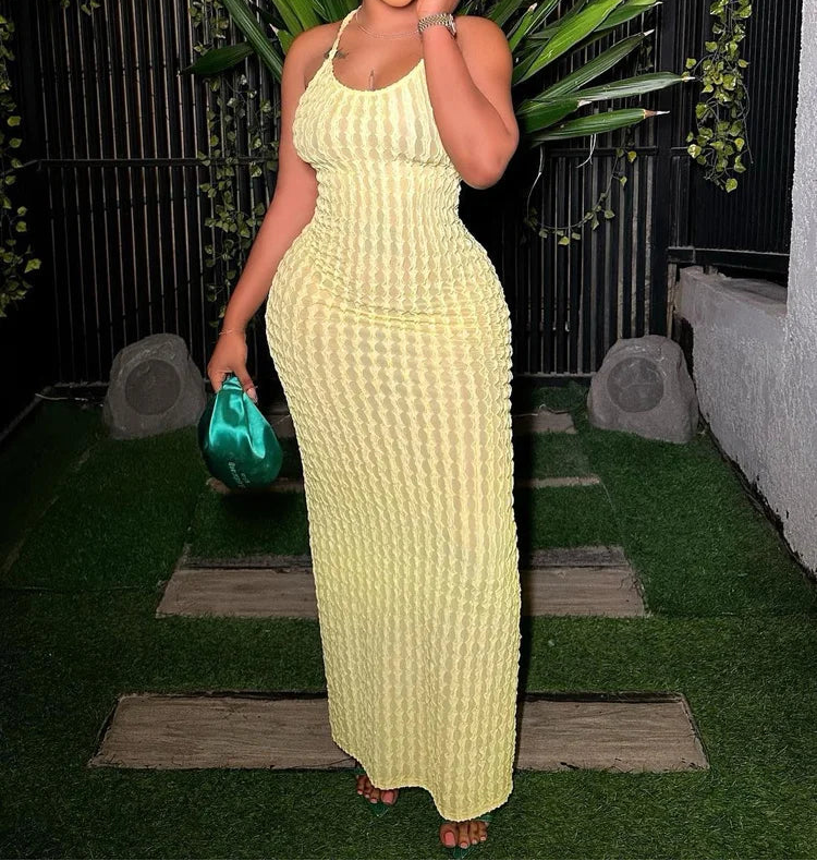 Woman in a yellow dress holding a green clutch against a dark background with plants.