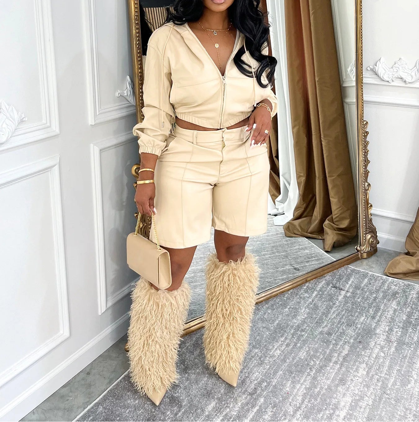 Woman in a beige outfit with fur boots standing in front of a mirror.