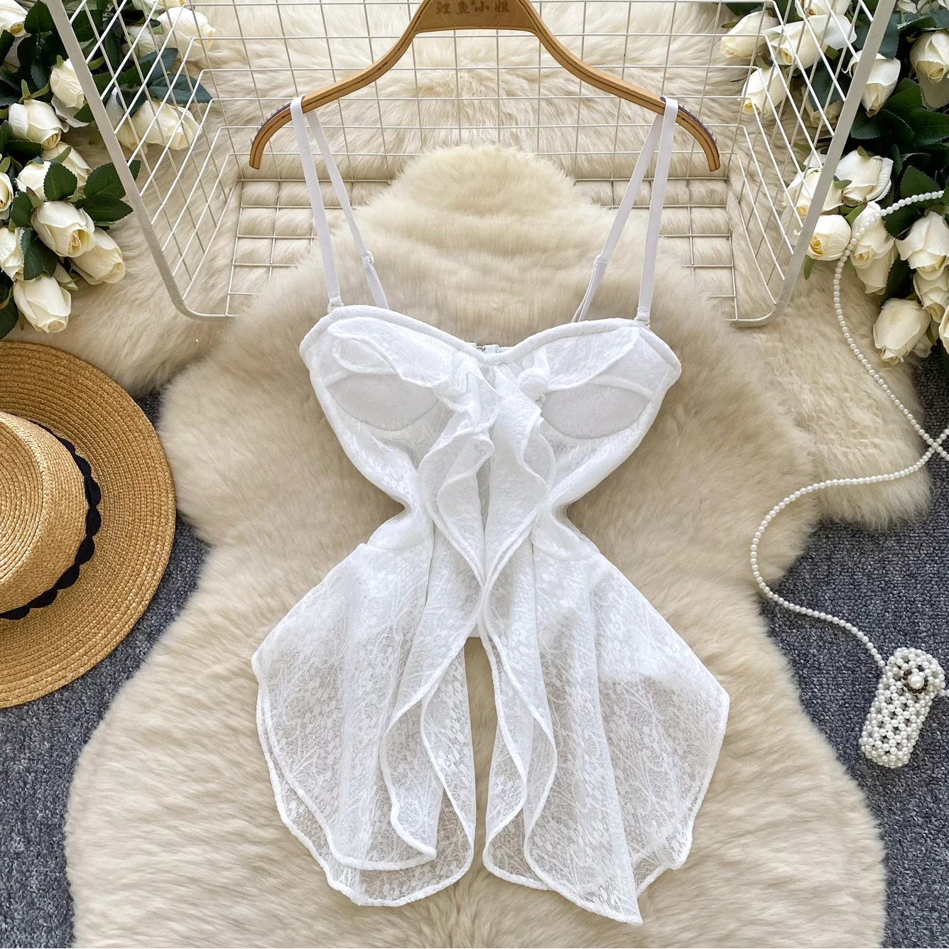 White lace top on a hanger with decorative flowers and a hat in the background
