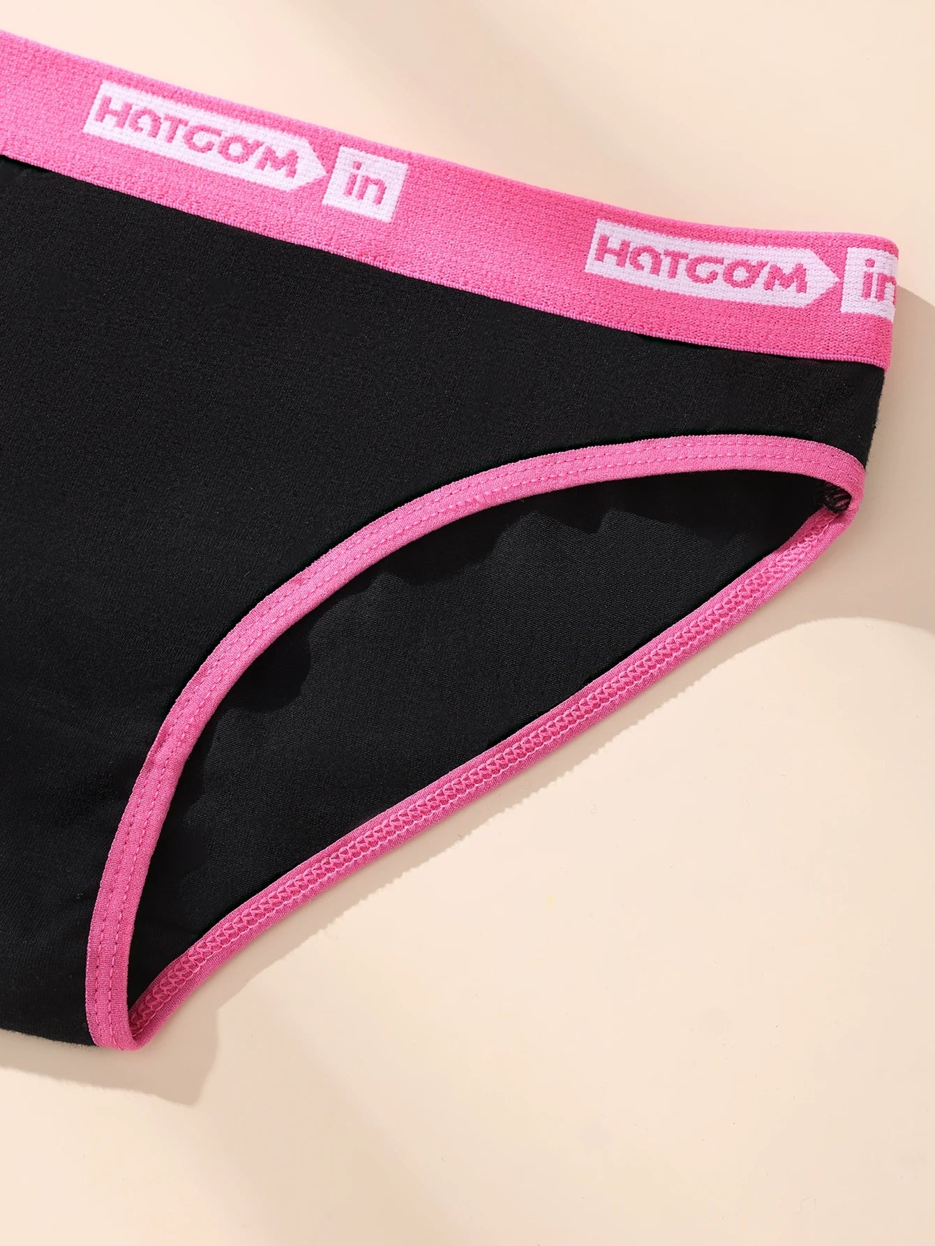 Black underwear with pink waistband featuring 'HOTGOM' branding on a beige background