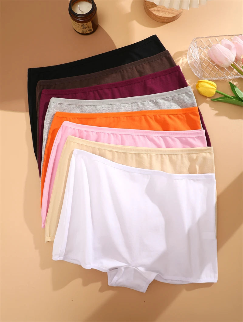 Set of colorful underwear on a beige surface with a candle and flowers in the background.