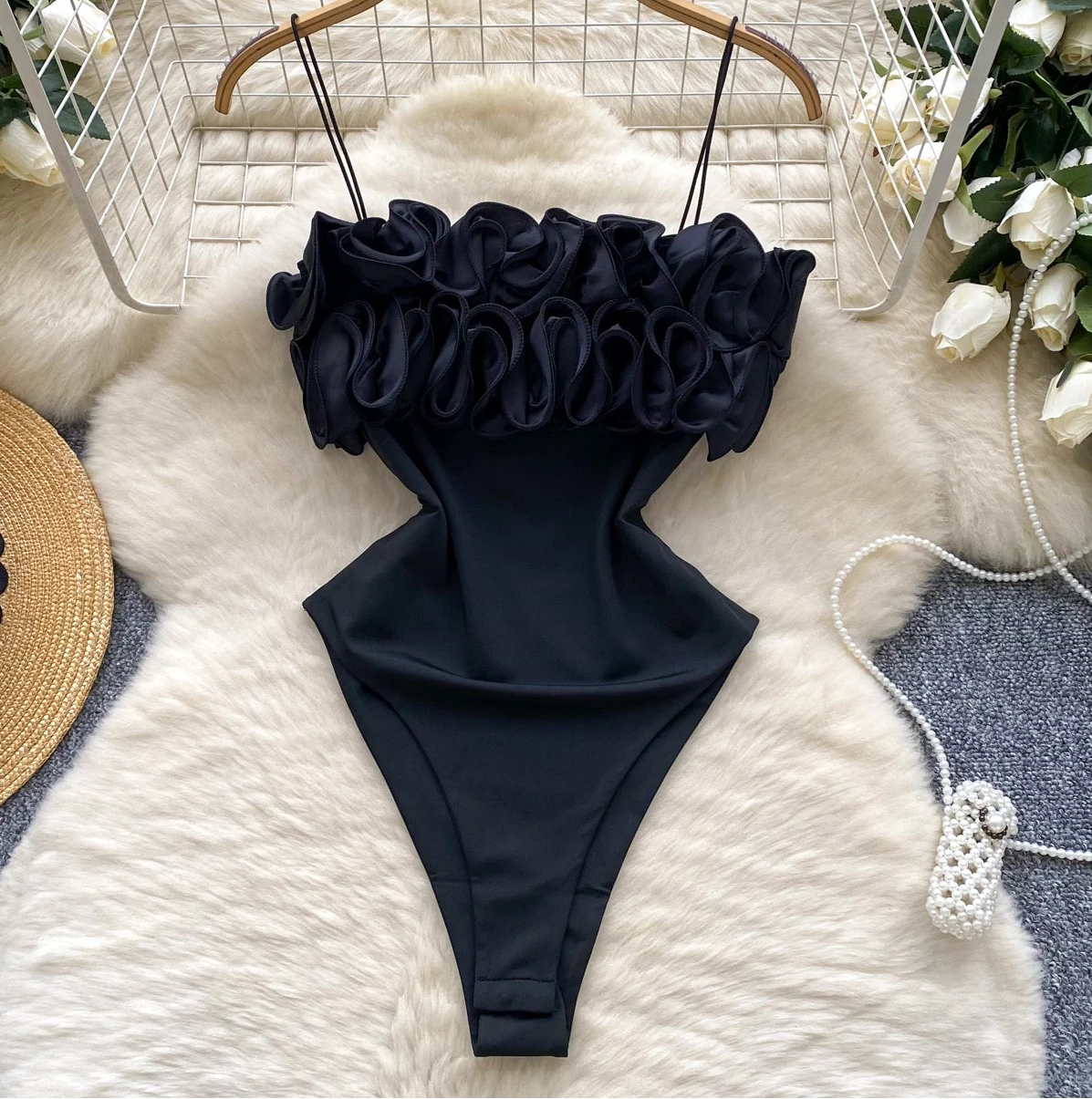 Black swimsuit with ruffled top on a white fur rug surrounded by decorative items.