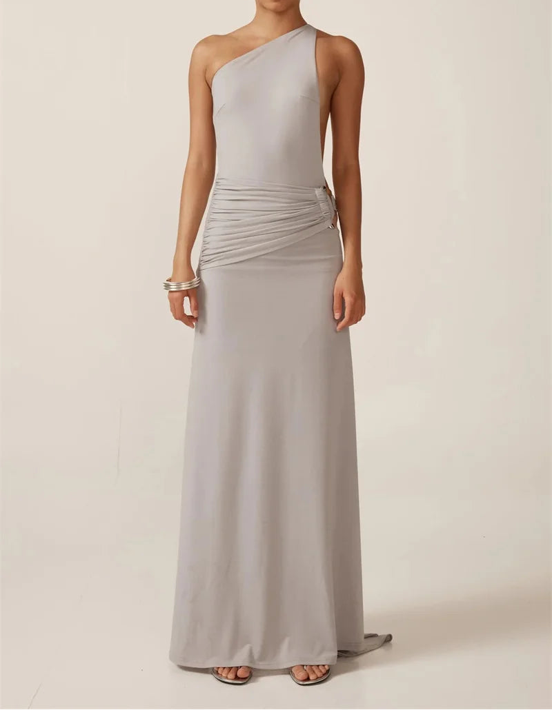 Woman wearing a long, light gray one-shoulder dress against a plain background