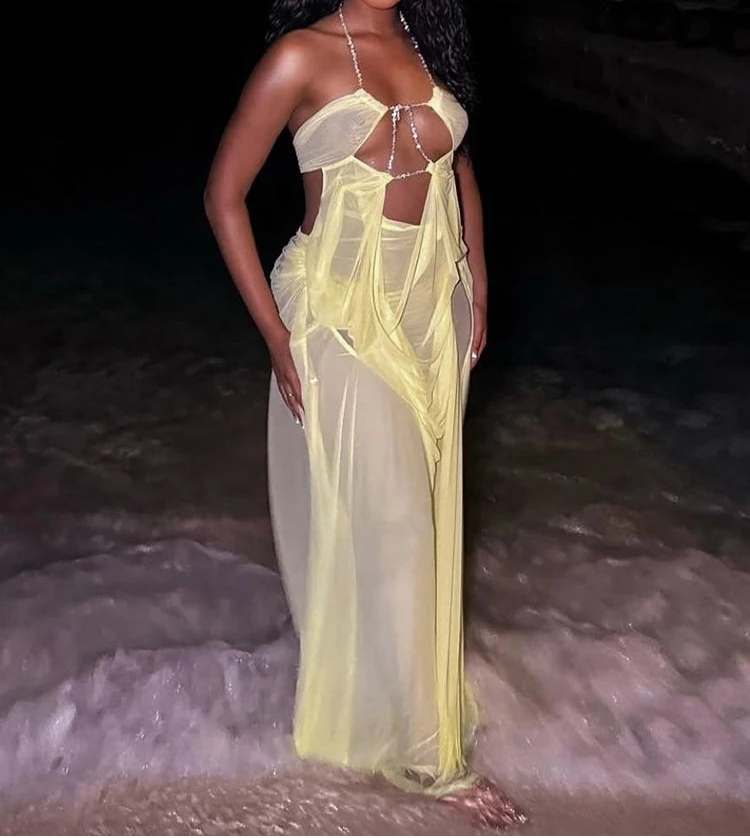 Woman in a sheer yellow dress standing on a rocky beach at night.