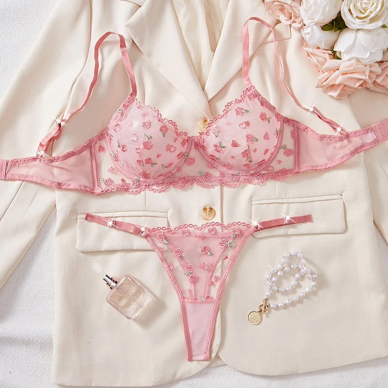 Pink lingerie set with a blouse, floral arrangement, and perfume bottle on a white background