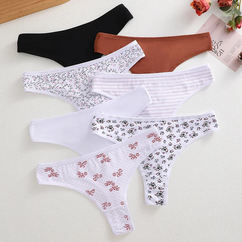 Five pairs of women's thong underwear arranged in a flat lay on a light textured surface. The set includes black, rust brown, white with small floral print, white with thin stripes, and white with embroidered butterfly details.