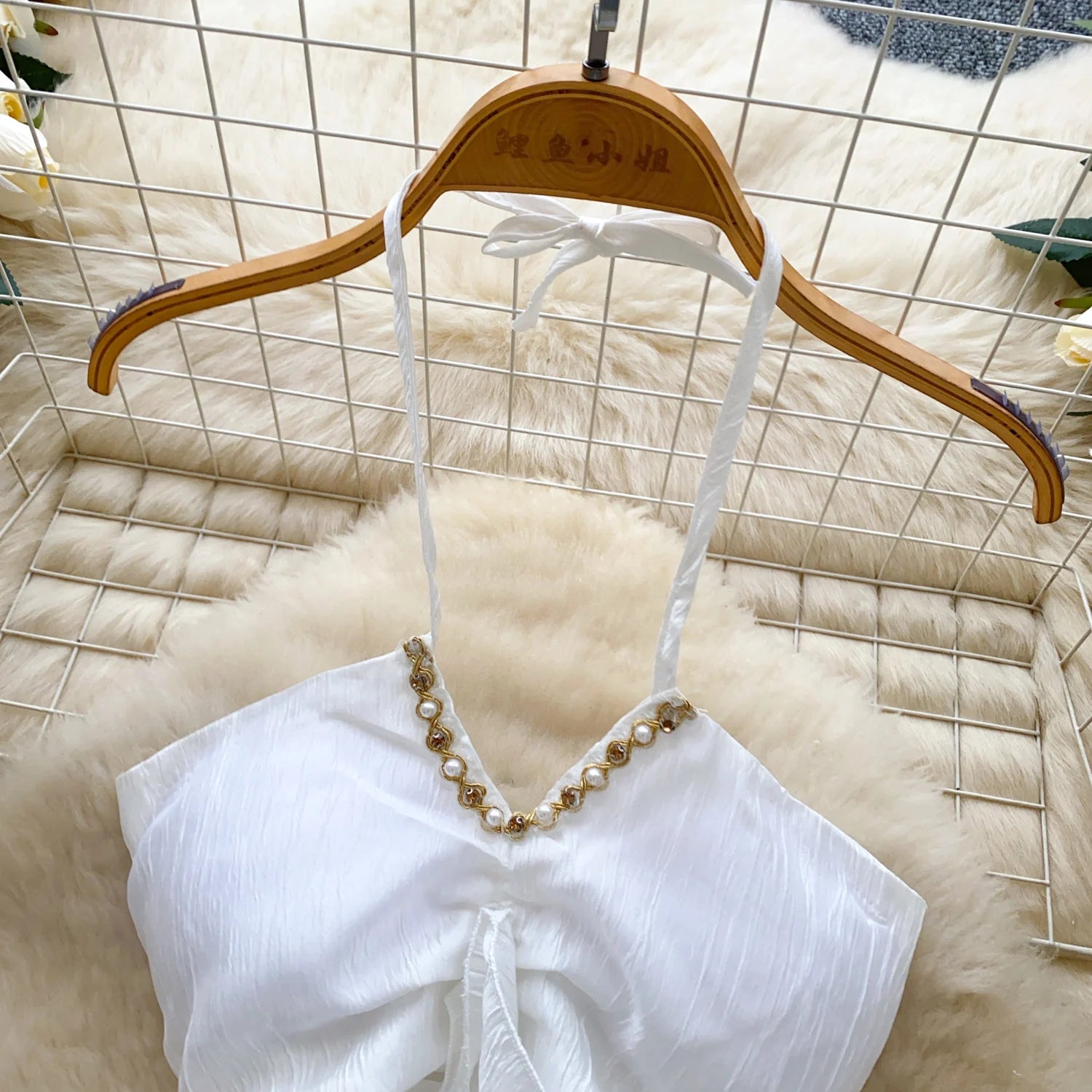 White top with pearl embellishments on a wooden hanger against a textured white background