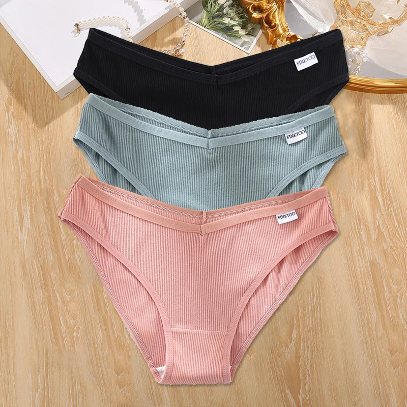 Three pairs of ribbed underwear in black, gray, and pink on a wooden surface.