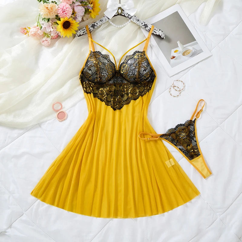 A yellow lingerie chemise dress with a black lace bust and matching black lace thong, arranged on a white quilted bed with flowers, jewelry, and a small photo frame as props.