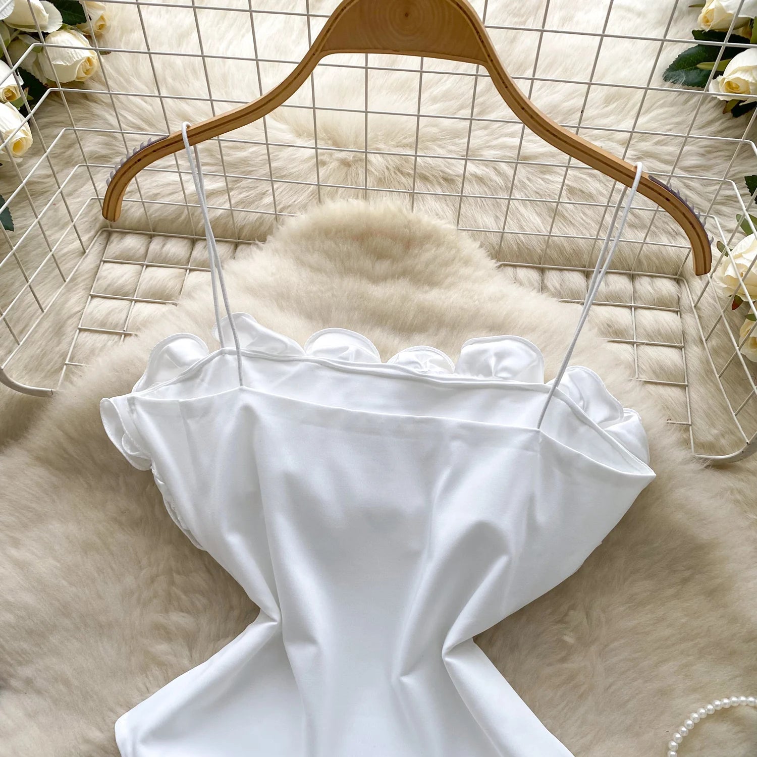 White dress on a wooden hanger against a light background with flowers.