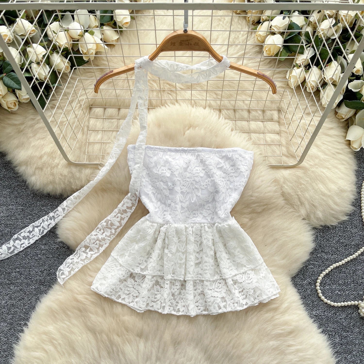 White lace dress on a hanger against a decorative background with flowers and a fur rug.