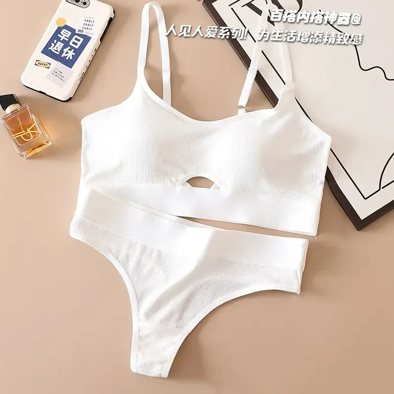 White bikini set on a beige surface with a phone, perfume bottle, and framed picture in the background.