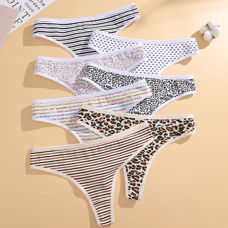 Six pairs of women's thong underwear arranged in a fan-like flat lay on a warm beige background. The styles include black and white stripes, white with small black hearts, beige and white leopard print, black and white leopard print with thin multicolor stripes, brown and black leopard print, and brown and black stripes.