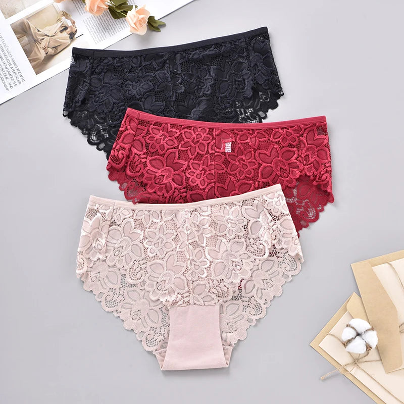 Three pairs of lace underwear in black, red, and beige on a gray surface.