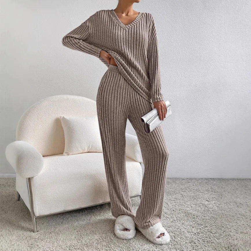 Person wearing a ribbed knit outfit standing in a minimalistic room with a white chair.