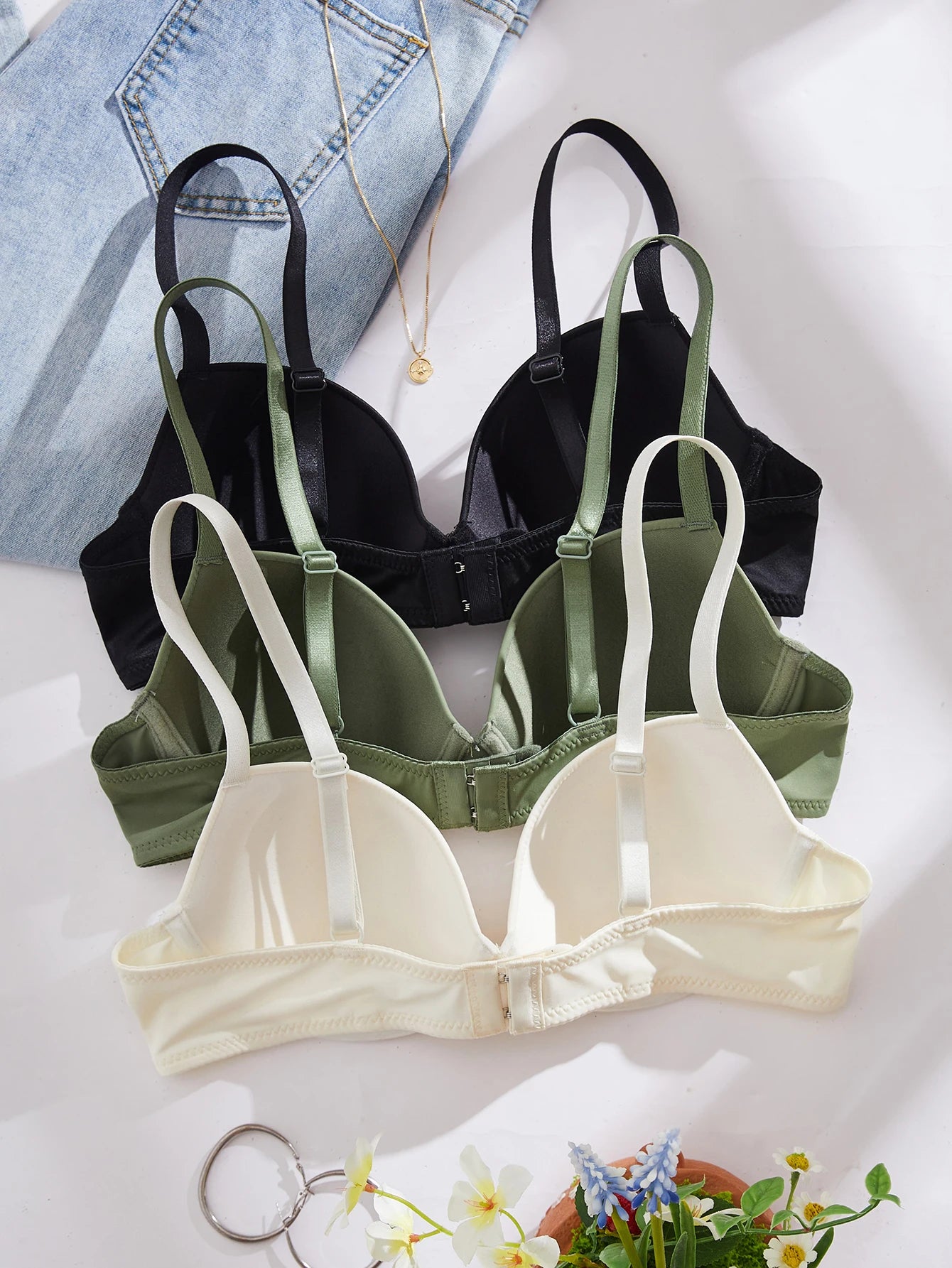 Three bras in black, green, and beige on a light background with denim jeans and flowers.