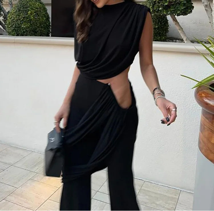 Woman in a black outfit standing outdoors with a building and plants in the background