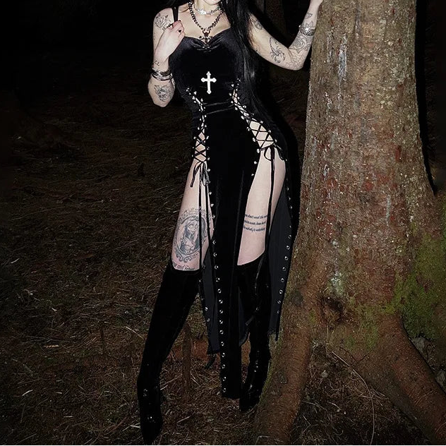 Woman in a black outfit with tattoos standing next to a tree in a dark forest