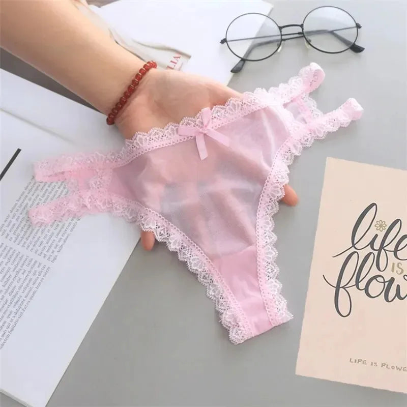 Pink lace lingerie held by a hand on a surface with books and glasses.