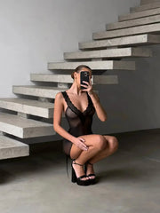 Person in black lingerie taking a mirror selfie against a modern staircase.
