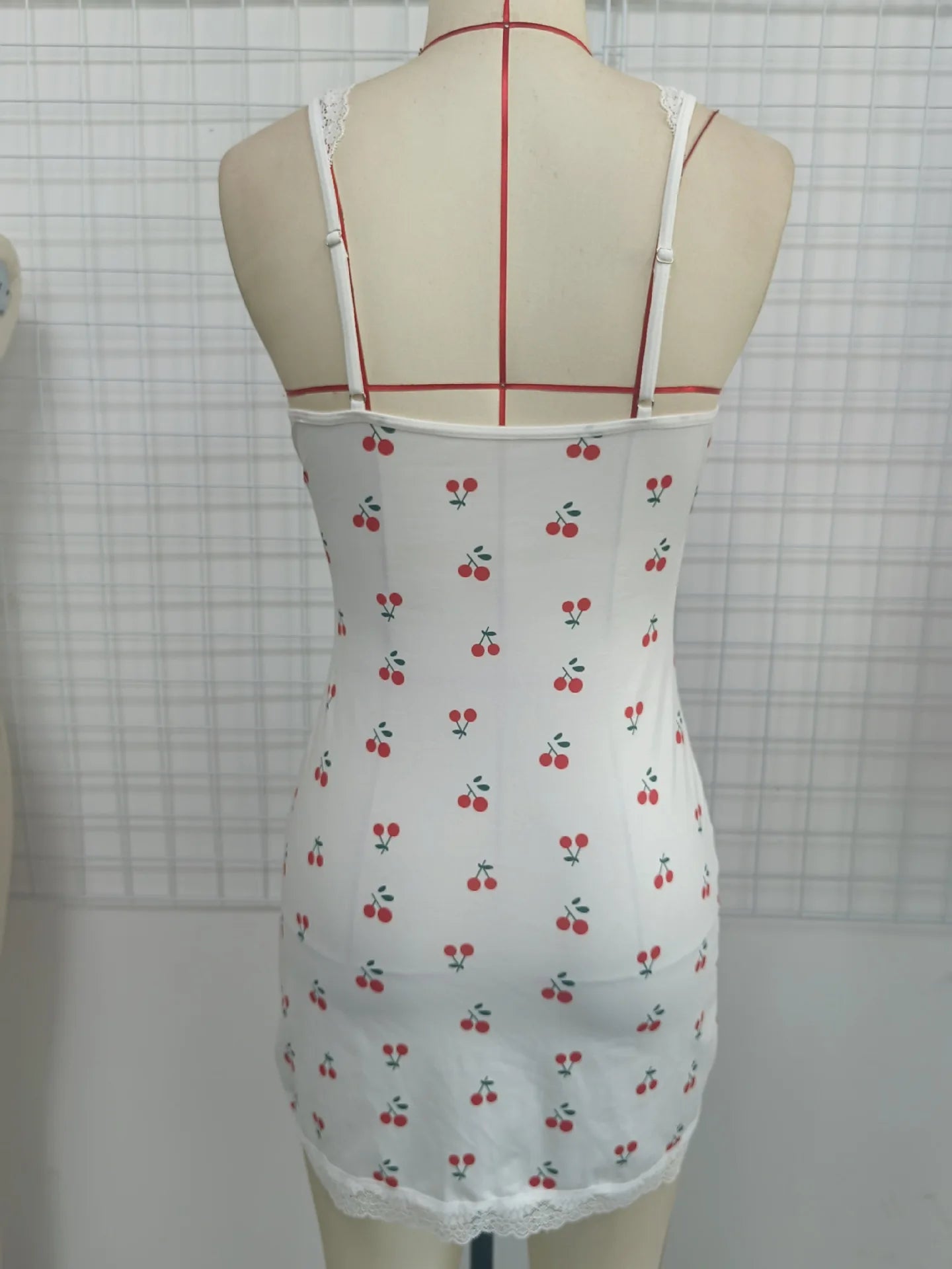 White dress with cherry pattern on a mannequin against a grid background