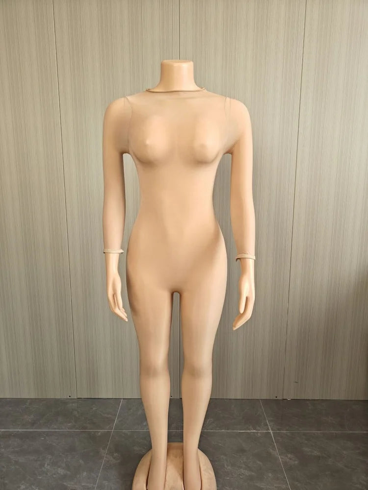 A full-body female mannequin dress form with a smooth beige skin-like finish, standing against a light wood-paneled wall and dark gray tiled floor.