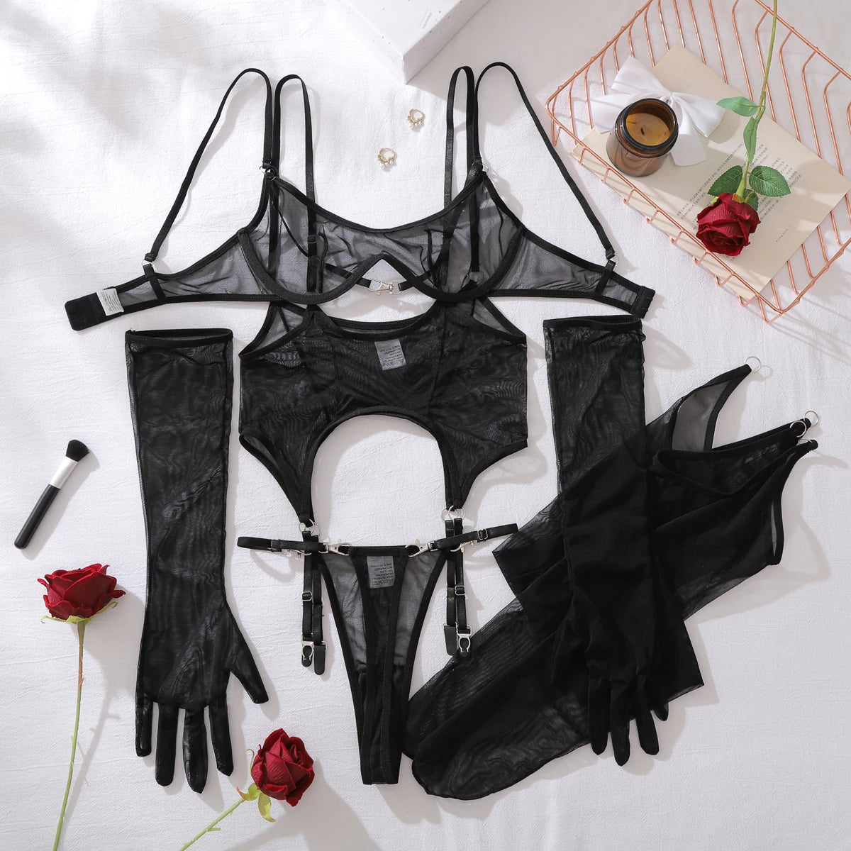 Black lingerie set with garters and gloves on a white surface with roses and a candle.