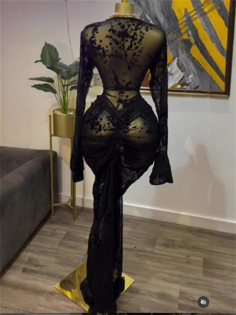 Mannequin wearing a black lace dress in a room with a couch and plant.