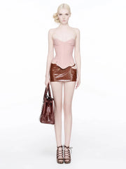 Model wearing a pink top and brown leather skirt with a handbag on a white background