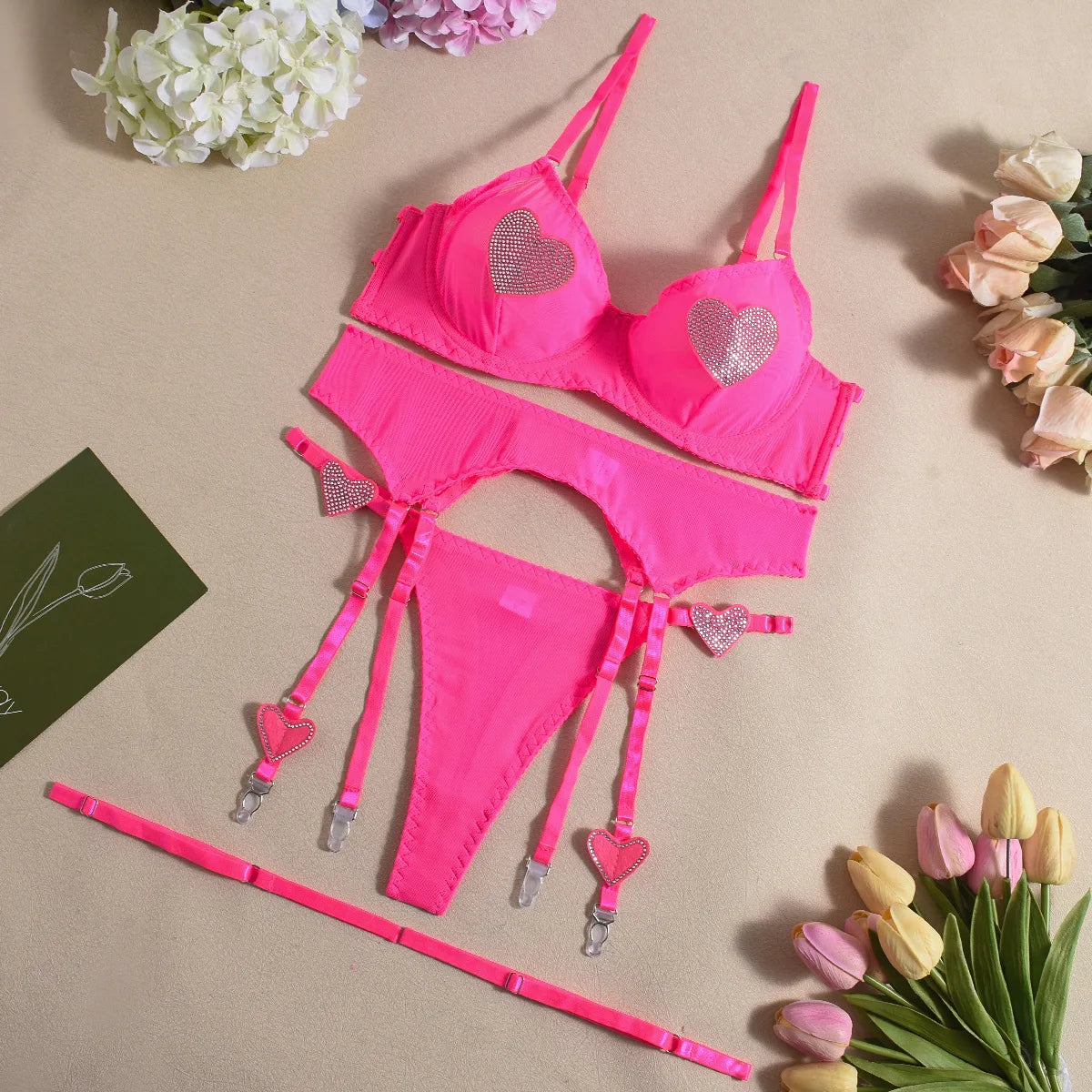 Pink lingerie set with heart details on a beige background with flowers.