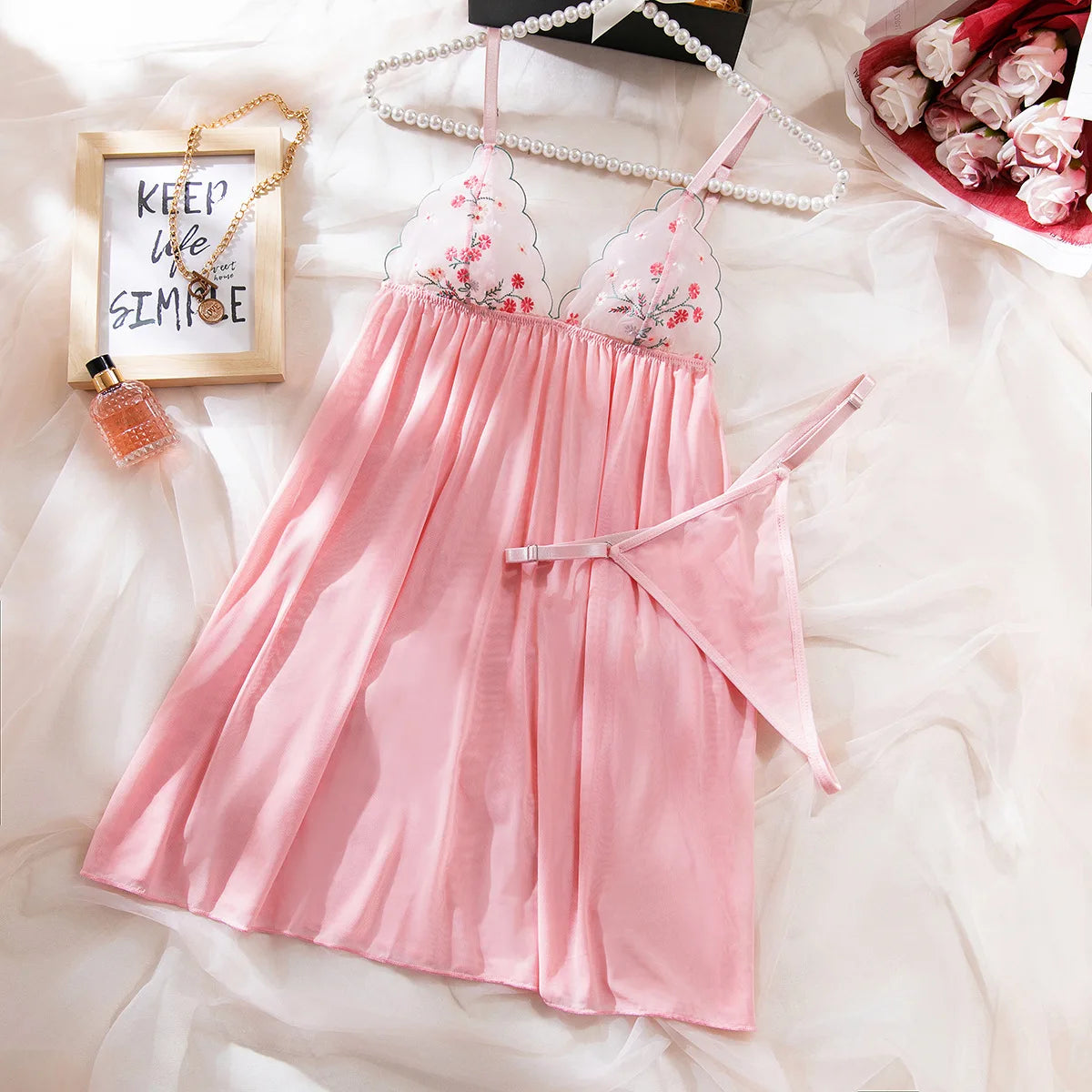 Pink dress with floral lace details on a white surface with decorative items.