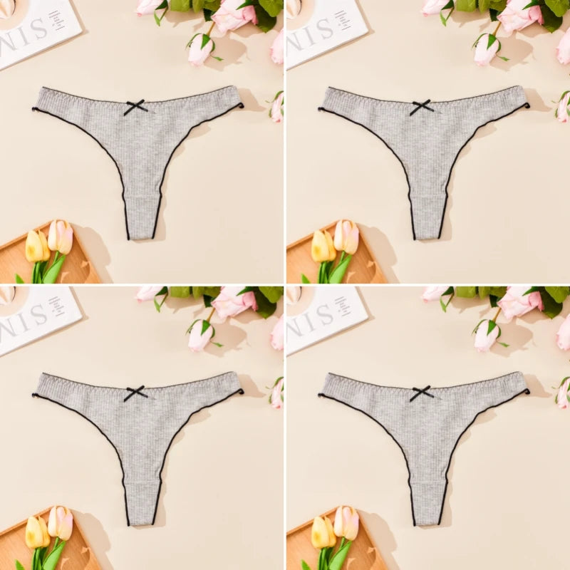 Gray thong with black bows on a beige surface with flowers and stationery.