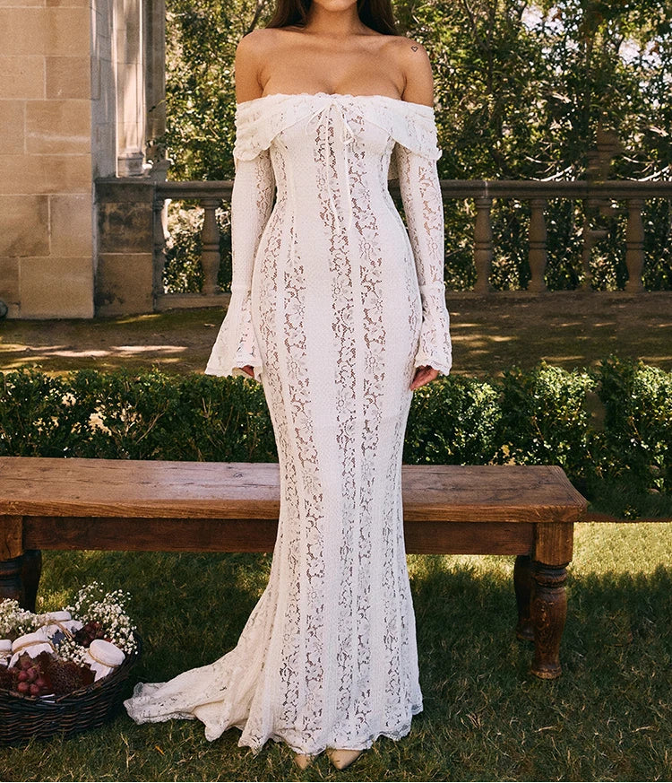 Woman in a white lace off-shoulder dress standing outdoors near a wooden bench.