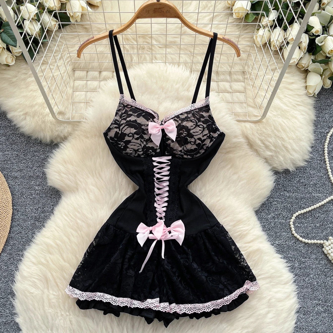 Black lace lingerie set with pink bows on a hanger against a floral and rug background