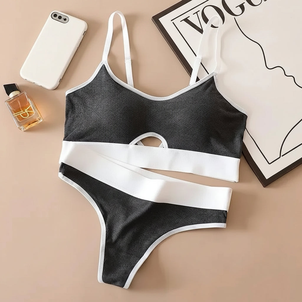 Black and white bikini set on a beige surface with a phone, perfume bottle, and box in the background.