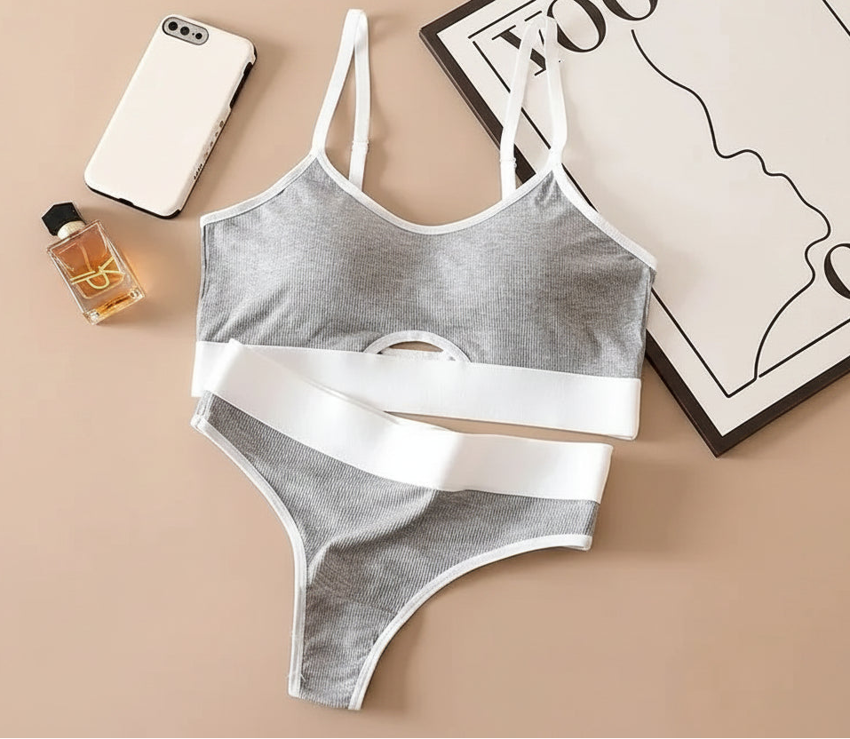Gray and white bra and panties set on a beige surface with a phone and perfume bottle.