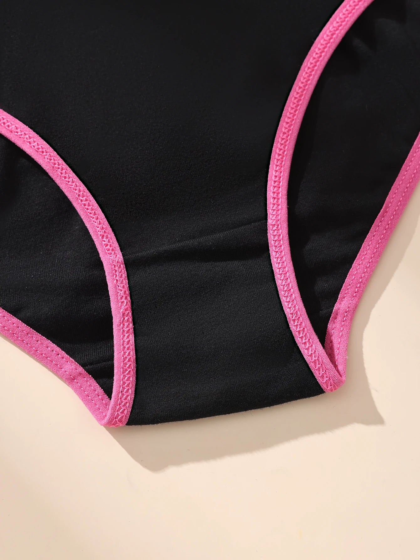 Black swimsuit with pink straps on a beige background