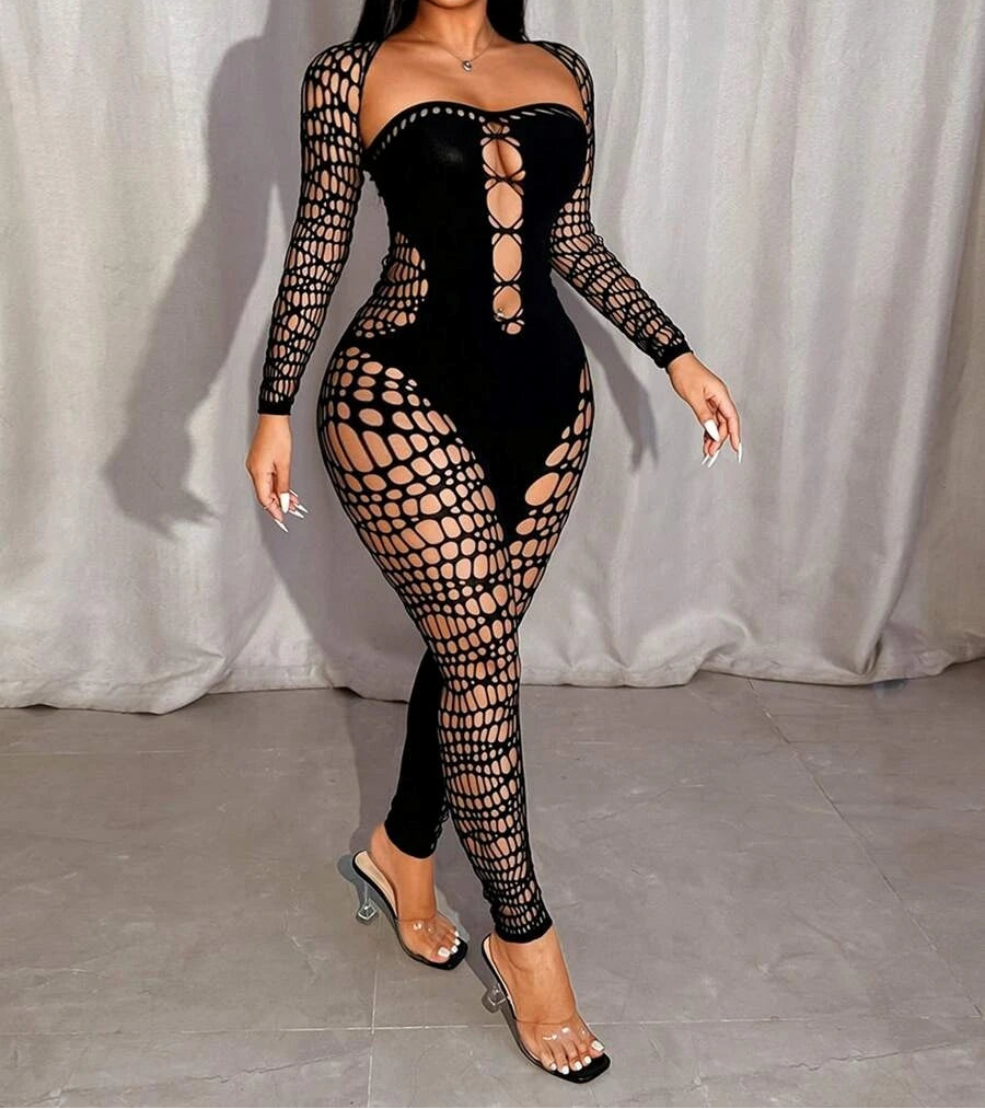 Model wearing a black fishnet outfit with long sleeves and sheer panels against a white curtain background.