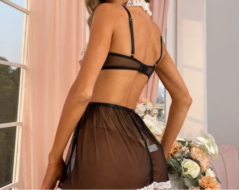 Woman wearing a black lace lingerie set in a softly lit room with pink curtains.