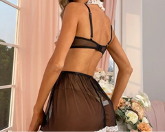 Woman wearing a black lace lingerie set in a softly lit room with pink curtains.