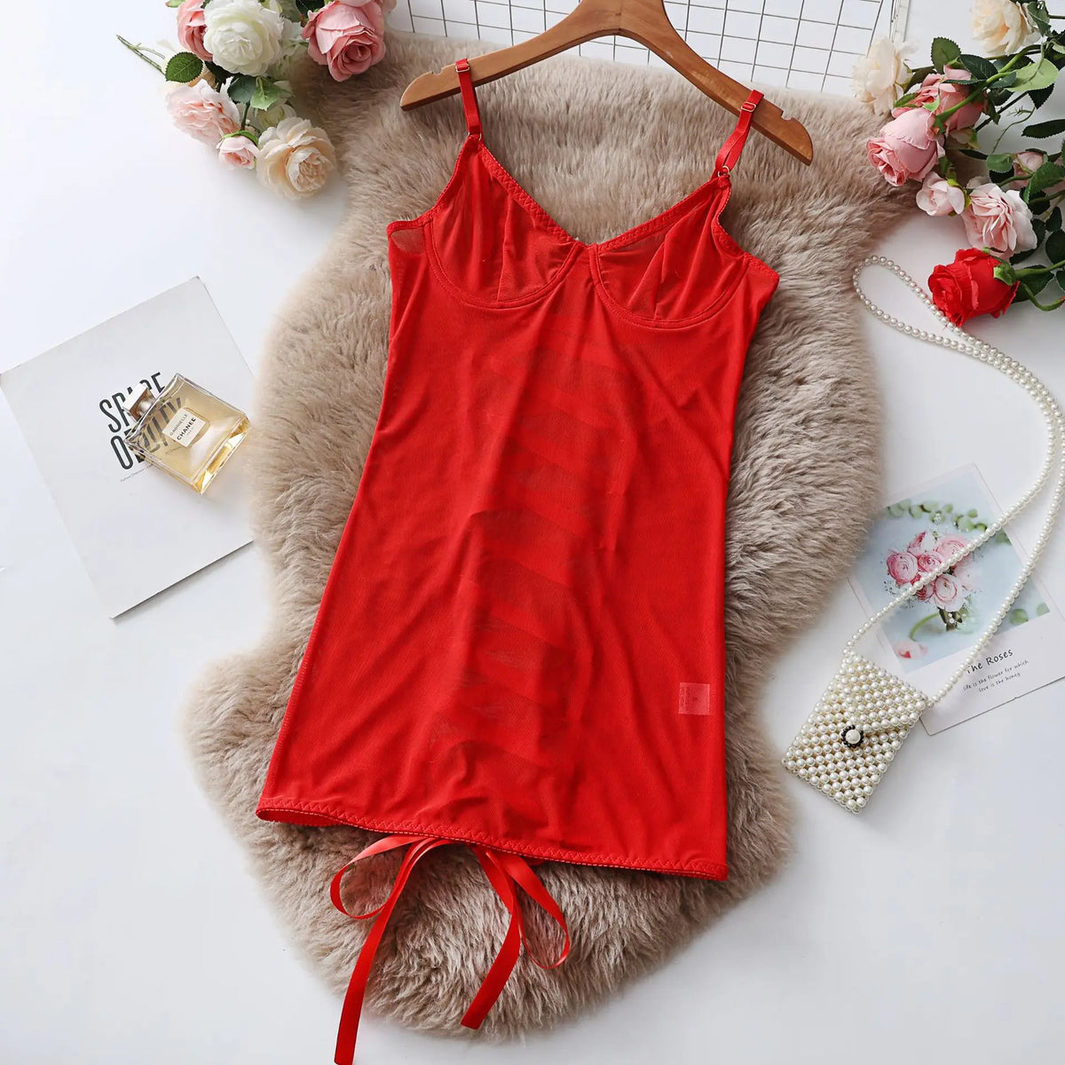 Red camisole on a hanger with flowers and perfume bottle in the background