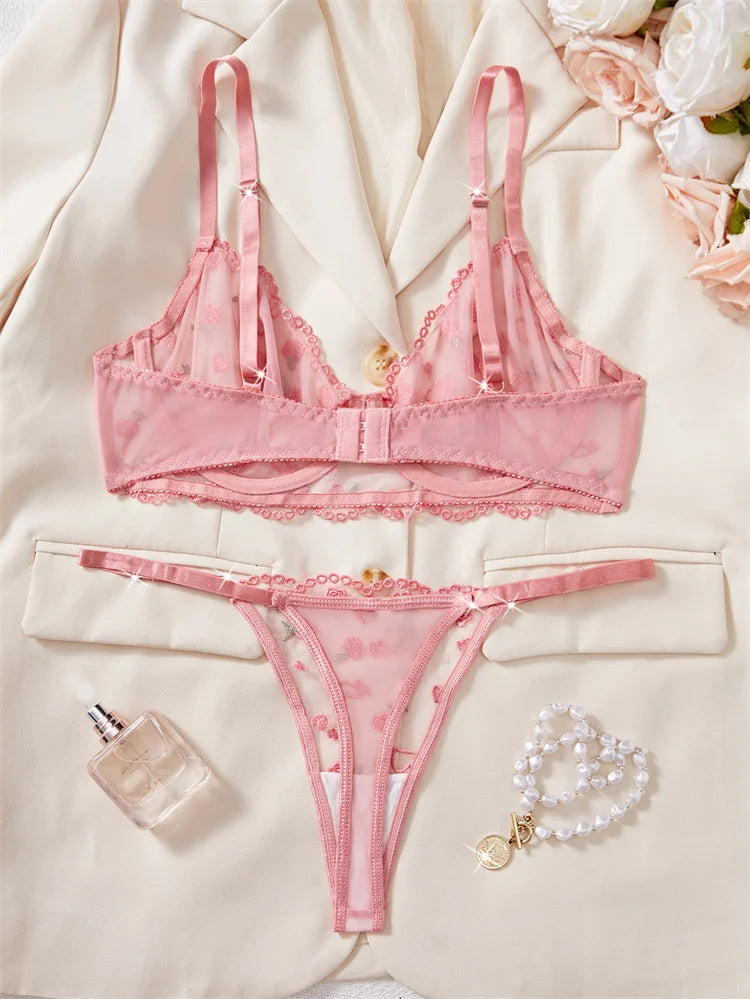 Pink lingerie set with a bottle of perfume and bracelet on a light background