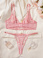 Pink lingerie set with a bottle of perfume and bracelet on a light background