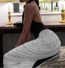 Woman in a black top and white skirt sitting on a chair in a room with lamps and a mirror.