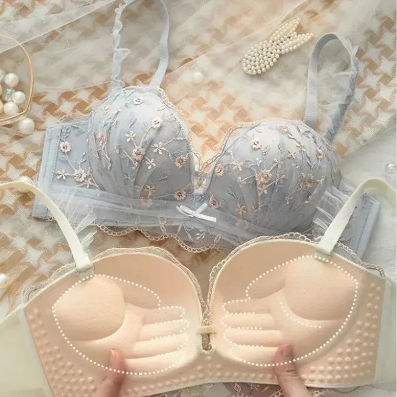 Two bras, one light blue with floral embroidery and the other beige, on a textured surface.