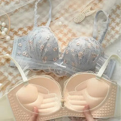 Two bras, one light blue with floral embroidery and the other beige, on a textured surface.