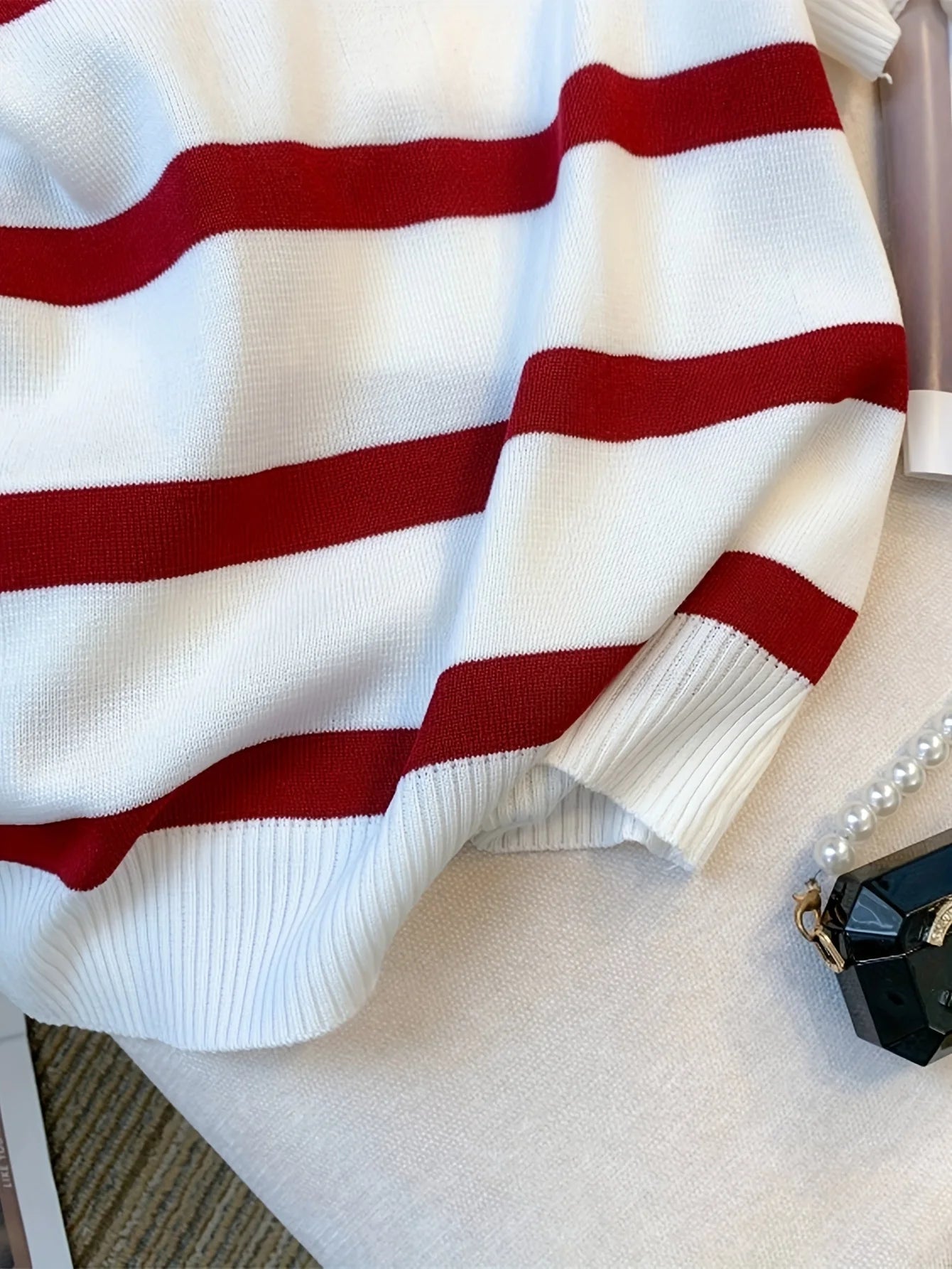 Close-up of a white sweater with red stripes on a light gray surface.